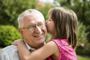 A little girl leaning over to whisper secrets in her grandfather’s ear as he smiles in delight. Better hearing makes listening fun.