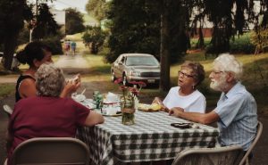 man in white crew neck t-shirt sitting on chair in front of table with food
