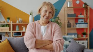 Home improvements for seniors. Image: Smiling elderly woman with arms crossed in living room.